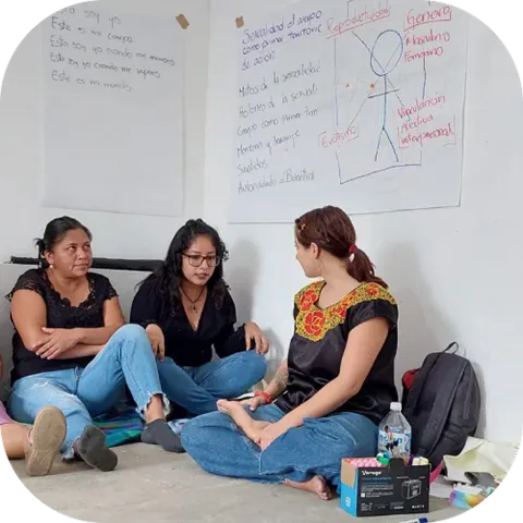 Tres mujeres conversan sentadas en el suelo durante un taller